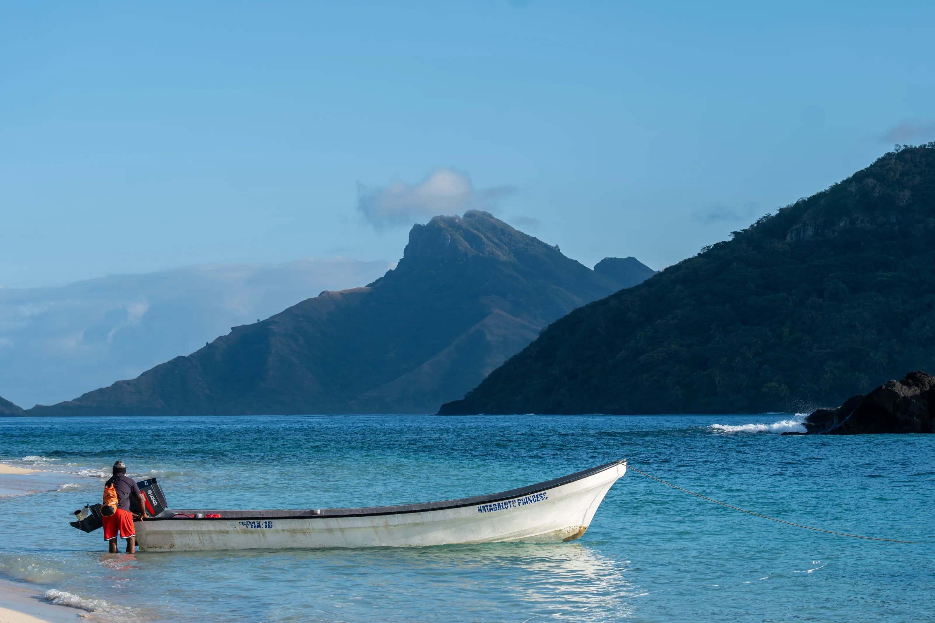 An island boat in clear blue water beneath Fiji’s coastal mountains